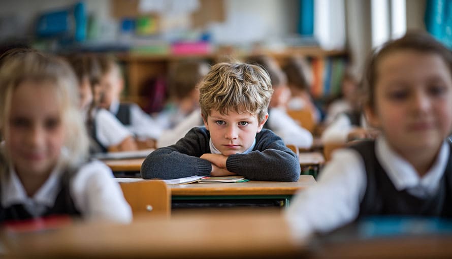 smutný chlapec sedí v školskej lavici medzi šťastnými spolužiakmi