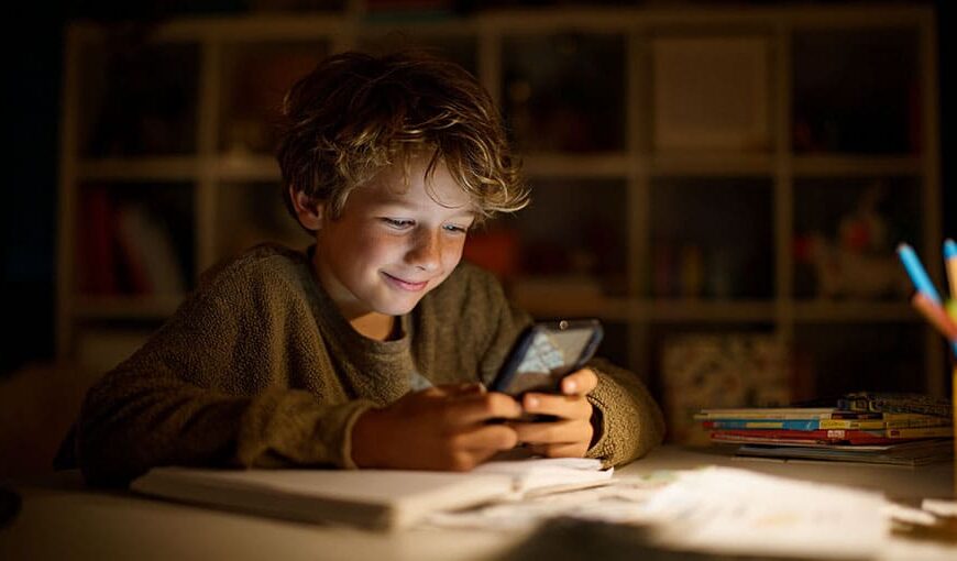 Chlapec sedí v prítmí svojej izby za stolom a pozerá do mobilu ktorý mu ožaruje tvár